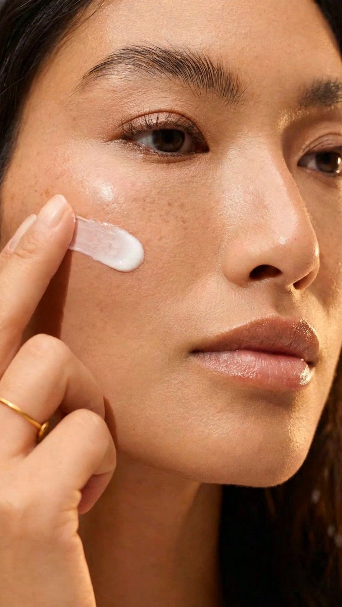 Close-up of woman applying luxury holistic face cream to cheek in a warm natural light skincare routine